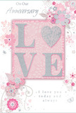 The anniversary card in the image is designed as a gentle celebration of enduring romance, using a soothing palette of pastel pinks, dove greys, and shimmering silver that would sit beautifully on a mantelpiece in any Woodford home. At its heart, the word LOVE is spelled out in softly raised glitter letters, each stroke edged with sparkle that catches the light as you tilt the card. The letter O is transformed into a glistening silver heart, textured so that it appears almost like pressed metal or a finely foiled embellishment, giving the centre a focal point rich in sentiment. Around this central word, delicate blooms in blush and mauve unfold with a watercolour softness, their petals gently shaded to suggest depth without heaviness. Their stems curl into graceful swirls and loops, reminiscent of the fluid lines a local florist might use when designing a romantic bouquet for delivery across Woodford, Buckhurst Hill, or South Woodford. Tiny flourishes-floating petals, light spirals, and barely-there butterflies-create a sense of movement, as if a spring breeze were drifting in from nearby Epping Forest and carrying the flowers across the page. The phrases On Our Anniversary and I love you today and always are set in an understated, flowing script that harmonises with the curves of the vines. The composition feels intimate yet quietly celebratory, much like a private toast shared at home after flowers have been placed in a favourite vase. It is an ideal keepsake for honouring the shared journey of a couple whose love has grown season by season, as naturally as flowers opening to the Woodford light.